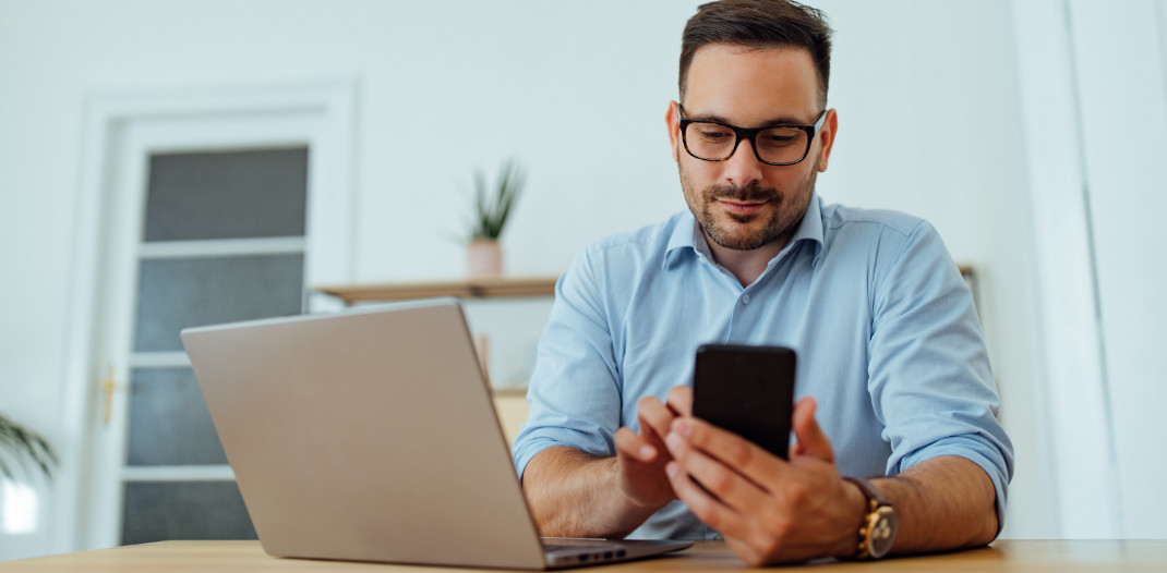 Man using social media on his phone whilst sat infront of a laptop