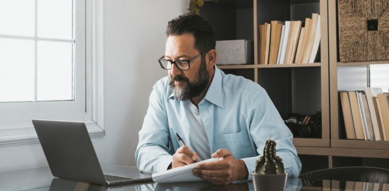 Man looking at laptop whilst taking notes